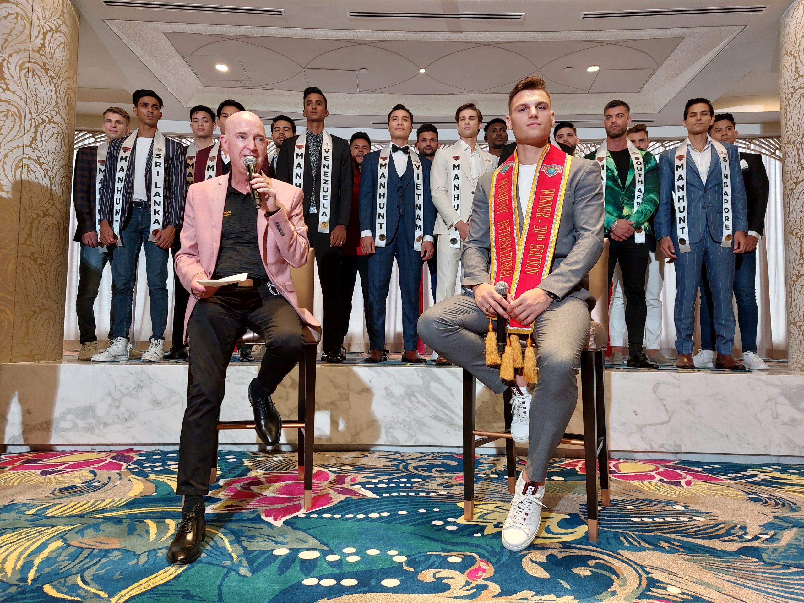 Manhunt International Executive President Rosko Dickinson (seated, left) joins current winner Paul Luzineau of the Netherlands (seated, right) at the presentation of the 2022 contestants
